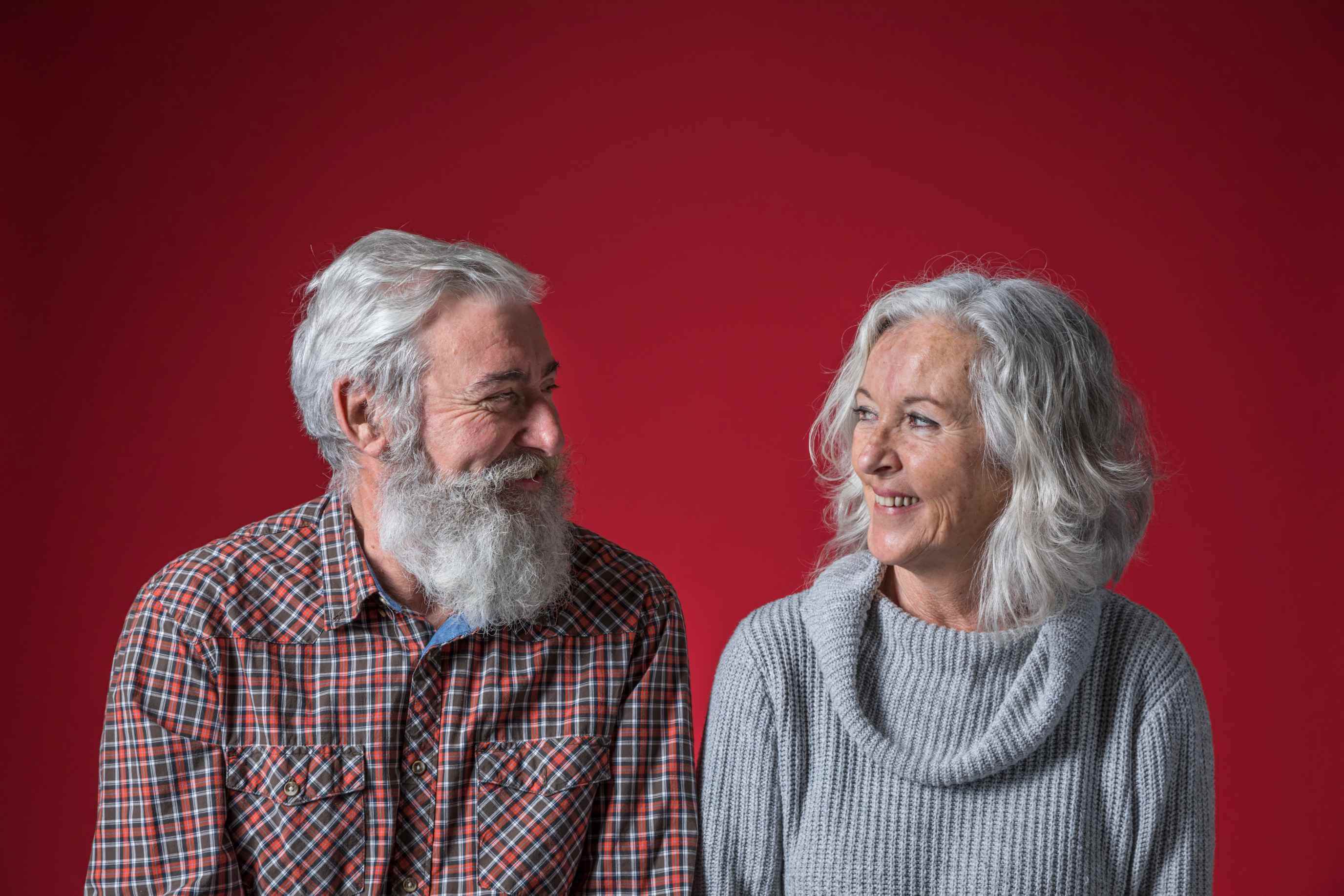 happy senior couple looking each other against red backdrop